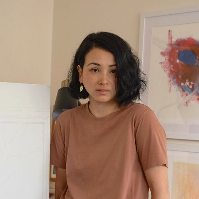 Mrs. Chen in her studio, with a framed red and blue abstract painting behind her