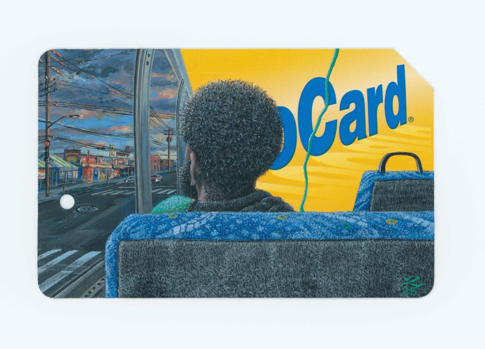 A passenger seen from behind on a bus with blue seats, looking out at a street at dusk