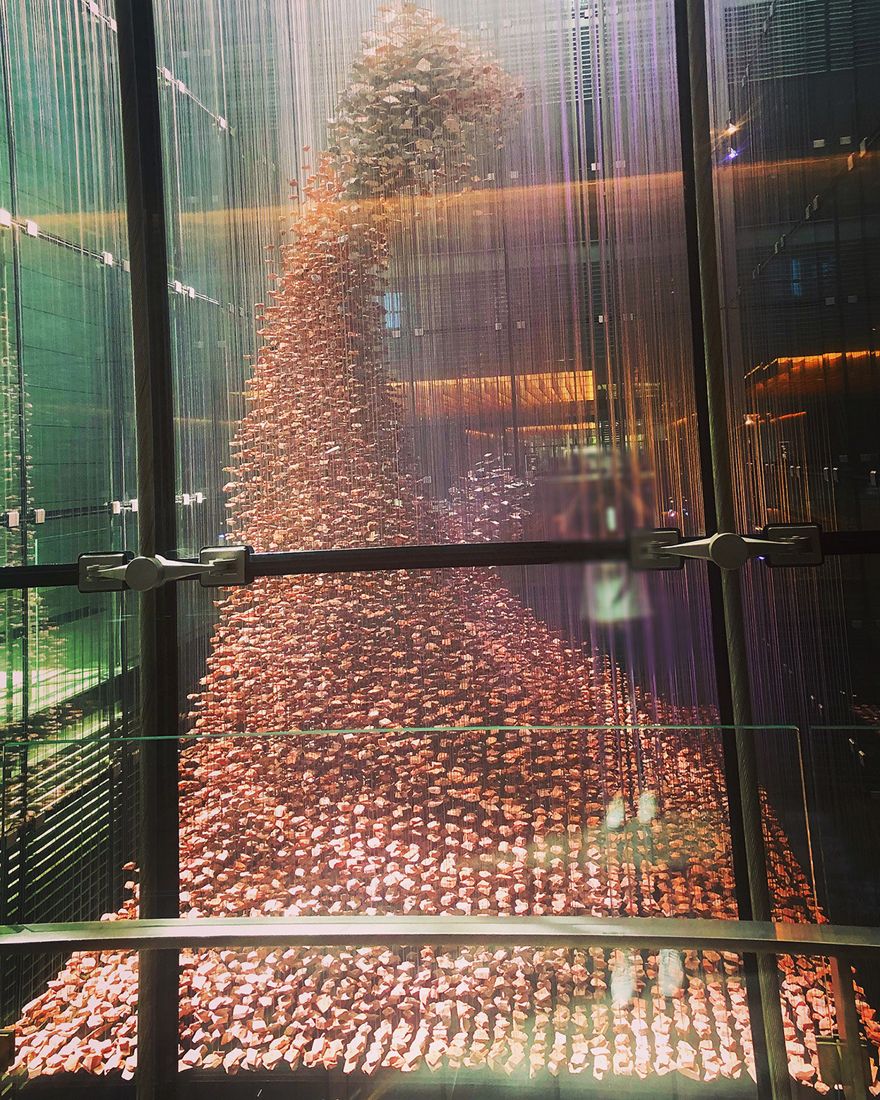A huge wave of hanging red bricks rising inside a tall glass atrium