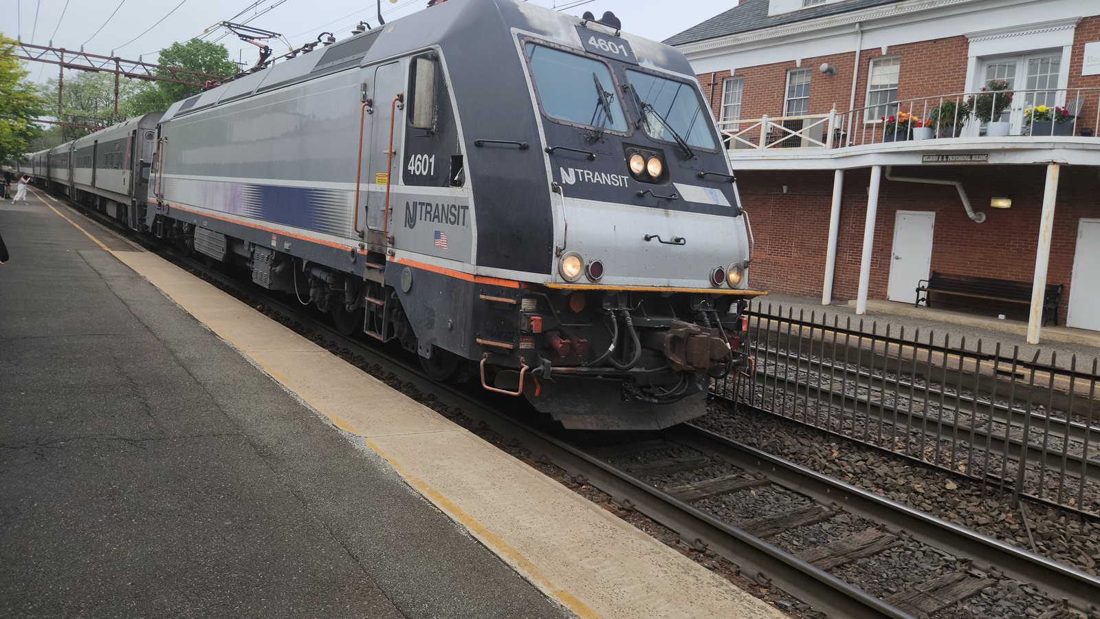 An NJ Transit train pulling into Millburn station, with the brick station building beside the platform